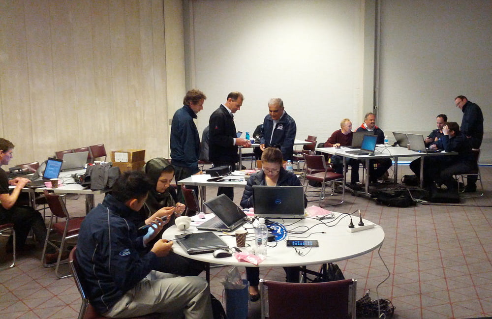 People in a conference room, working on laptops around tables