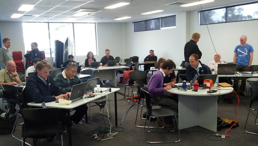 People in a conference room, working on laptops and with electronics hardware